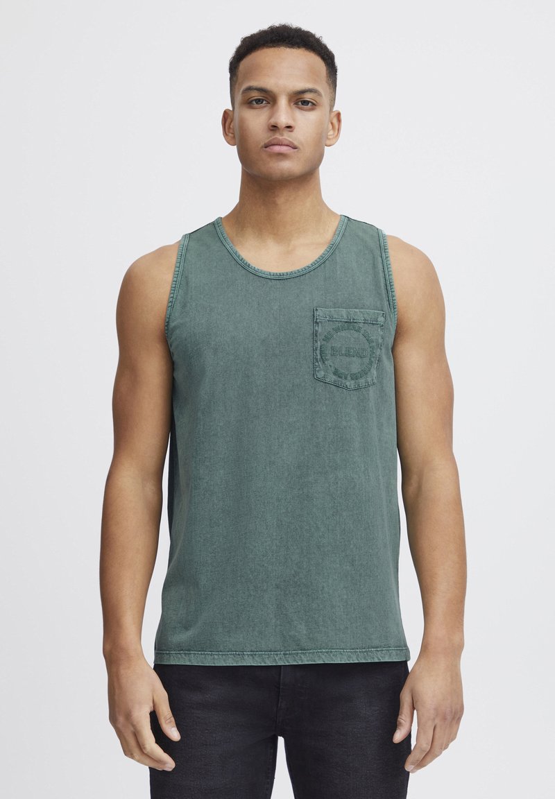 Top din denim verde cu decolteu rotund, având un buzunar pe piept cu inscripție embosată. Textură netedă și croială lejeră.