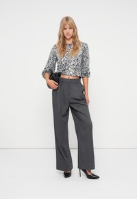 Strieborný flitrový crop top s dlhými rukávmi, v kombinácii s vysokými šedými širokými nohavicami a čiernymi lodičkami s ostrou špičkou.
