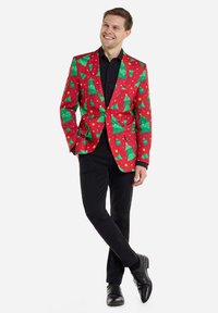 Rode blazer met een groen kerstboom- en sterrenpatroon. Zwarte shirt, zwarte broek en zwarte schoenen maken de feestelijke look compleet.