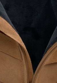 Brązowy zamszowy but z teksturowaną powierzchnią, z suwakiem po boku i ciemnym wnętrzem. Projekt jest prosty i funkcjonalny.