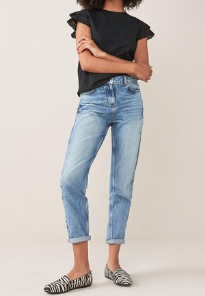 Haut noir à manches courtes avec bordure en dentelle, jean taille haute bleu clair avec revers, et ballerines rayées noir et blanc.