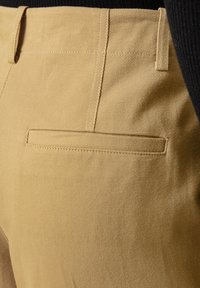 Khaki spodnie z teksturowanej tkaniny, z płaską tylną kieszenią, dopasowanym krojem i widocznym detalem szwów wzdłuż krawędzi.