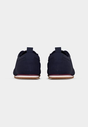 Paire de chaussures décontractées bleu marine vues de dos, avec des semelles blanches et marron et des languettes sur fond blanc.