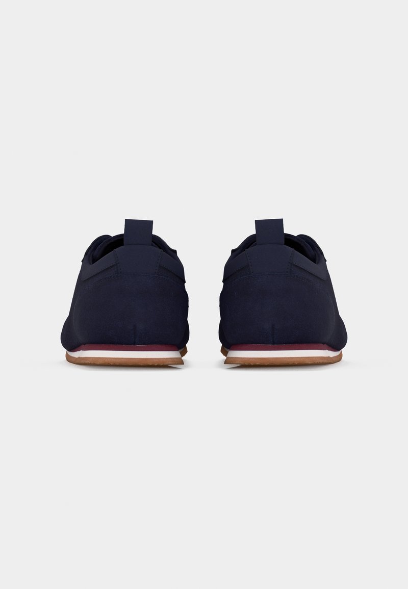 Paire de chaussures décontractées bleu marine vues de dos, avec des semelles blanches et marron et des languettes sur fond blanc.