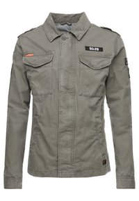 Grå militærstil jakke med to brystlommer, epaulettes og en frontknaplukning. Bemærkelsesværdige mærkater er placeret på brystet og skulderen.