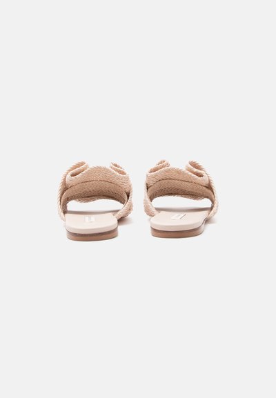 Επίπεδα μπεζ σανδάλια με πλεγμένους ιμάντες, που βλέπουμε από πίσω πάνω σε ένα απλό ανοιχτό φόντο.