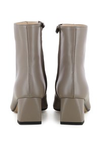 Beige nep leren enkellaarsjes met een vierkante blokhak, een gladde textuur en een rits aan de achterkant. De hakken zijn ongeveer 7,5 cm hoog.