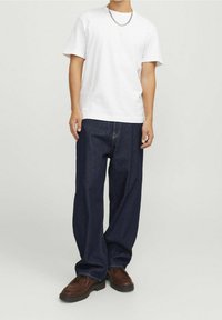 Vit bomullst-shirt, avslappnad passform, kombinerad med mörkblå denimbyxor. Bruna skor med en strukturerad yta, med en lågprofil design.