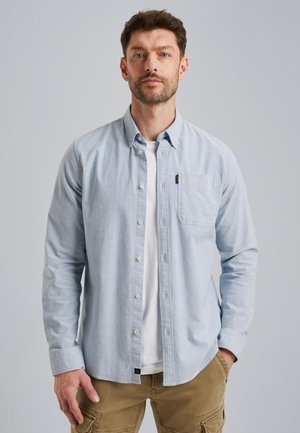 Lyseblå skjorte med knapper, lange ærmer, brystlomme, bomuldsstof, afslappet pasform. Båret over en hvid t-shirt, parret med beige cargobukser.