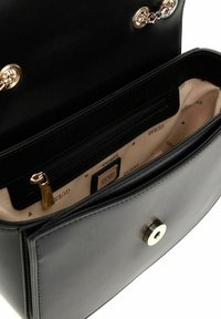 Sac à main en cuir noir avec des accessoires en ton or, présentant une chaîne décorative, une fermeture magnétique et un intérieur à motif beige.