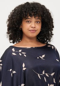Blusa navy in un tessuto morbido e fluido, caratterizzata da un motivo a foglie di colore chiaro. Collo rotondo e vestibilità ampia con maniche a tre quarti.