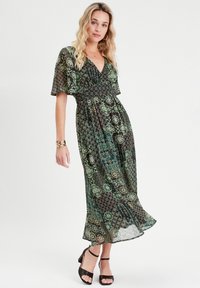 Robe maxi vert foncé avec des motifs floraux et géométriques. Légère, design à col en V, manches courtes et détail de taille froncée.