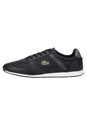 Baskets basses Lacoste noires avec semelle blanche, lacets noirs et logo crocodile vert sur le côté.