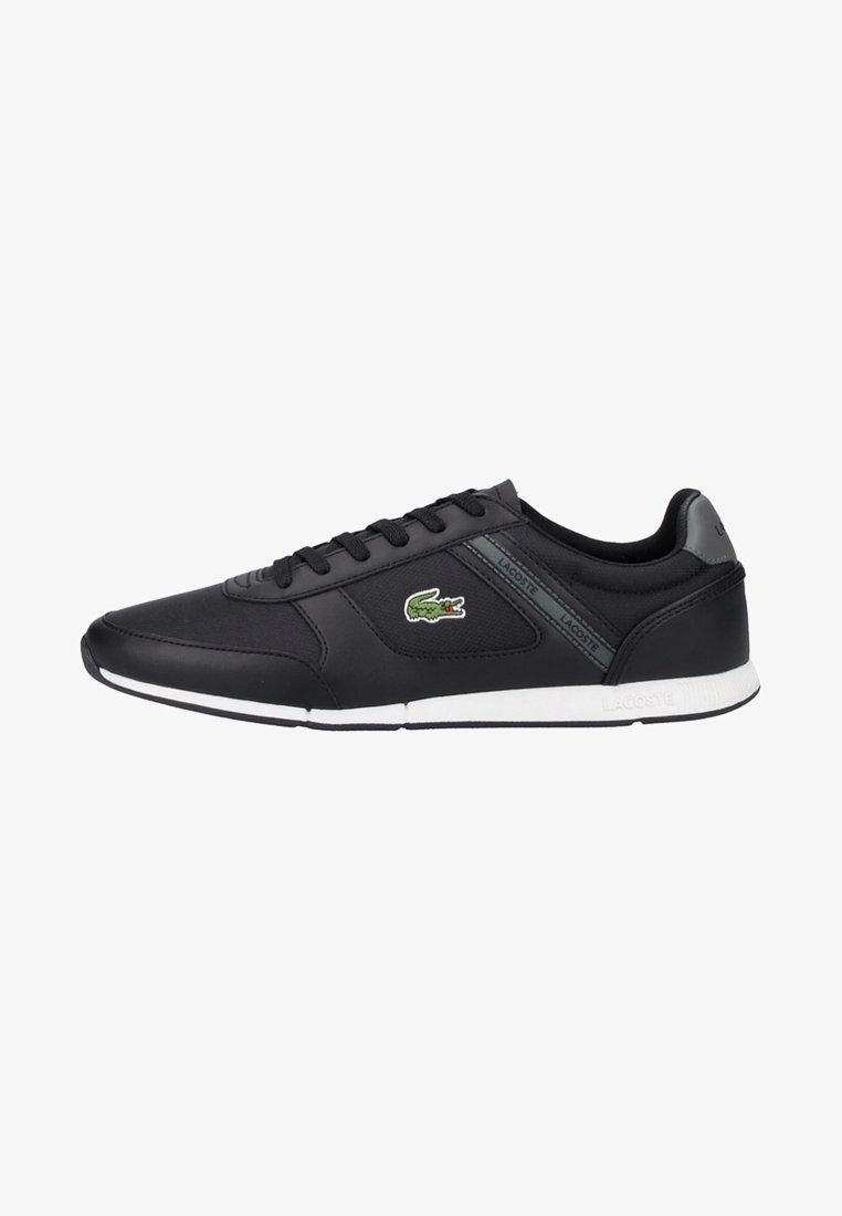 Baskets basses Lacoste noires avec semelle blanche, lacets noirs et logo crocodile vert sur le côté.