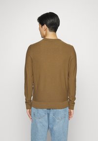 Brauner, gestrickter Pullover mit Rundhalsausschnitt und geripptem Saum. Lange Ärmel und strukturierte Oberfläche. Getragen mit hellblauen Jeans.