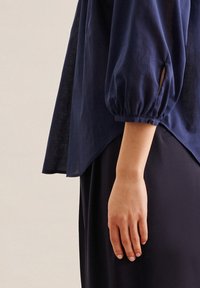 Marineblaue, leichte Bluse mit puffärmel, seitlichem Schlitz und Knopfdetails an den Manschetten. Weicher Stoff mit lässigem Schnitt.