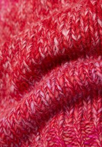 Roter Strickstoff mit unterschiedlichen Rot- und Pinktönen, der ein strukturiertes, ineinander verwobenes Muster und sichtbare Fasern für Weichheit aufweist.