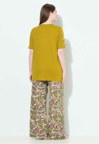 Krótka bluzka z krótkim rękawem w oliwkowej zieleni z kwiatowymi akcentami na rękawach, zestawiona z szerokimi spodniami w jaskrawym, wielokolorowym wzorze paisley.