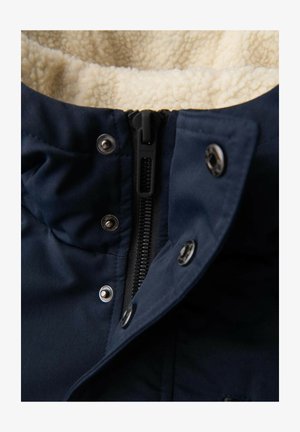 Giacca blu navy con interno in morbido pile color crema, chiusura con zip a vista e bottoni a pressione metallici lungo il colletto.