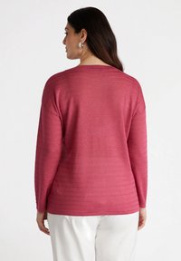 Maglione a maniche lunghe di un vivace colore rosa con un motivo a righe testurizzato. Presenta una vestibilità rilassata e un collo rotondo, abbinato a pantaloni bianchi.