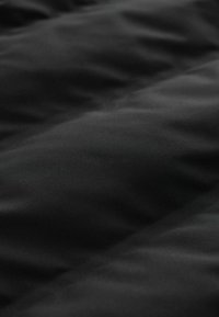 Schwarzer synthetischer Stoff mit einer glatten Textur, der leichte Falten und ein mattes Finish aufweist, was auf Weichheit und Wärme hinweist.