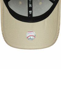 Bēša cepures vizieris ar melnu iekšējo odere un MLB hologrammas uzlīme centrā vīziera apakšā.
