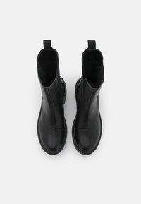 Botas de tobillo de cuero negro con una textura lisa, tiradores laterales y puntera redondeada. Suela plana y diseño minimalista.