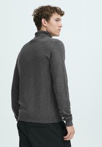 Mørk grå turtleneck genser med lange ermer, en tettsittende design og ribbestrikkede mansjetter. Stoffet har en myk tekstur og en subtil glans.
