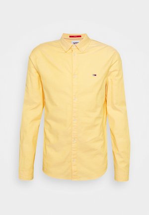Žlutá košile s dlouhým rukávem, límečkem, s malým logem Tommy Hilfiger na hrudi a knoflíky vpředu.