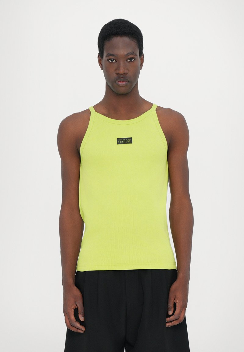 Limegrønn ribbestrikket tank topp med tynne stropper, med et svart logo merket på brystet. Slim fit design. Båret med svarte bukser.