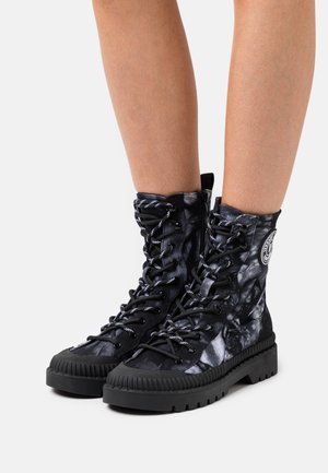 Zwart-grijs tie-dye combatboots met dikke zolen, veters aan de voorkant, zijritsen, gedragen op blote benen.
