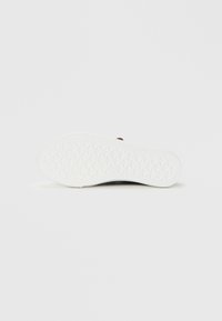 White rubber shoe sole with a patterned grip featuring geometric shapes. Minimal design, smooth texture, with stitching along the edge.