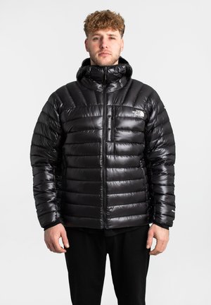 Czarna kurtka puchowa o błyszczącej powierzchni, poziomym pikowanym wzorze, samodzielnym kapturze i zamku błyskawicznym z przodu. Posiada kieszeń na piersi z logo.