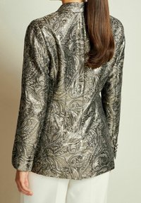 Giacca floreale a motivi metallici argentei e dorati con maniche lunghe, colletto alto e polsini con bottoni. Tessuto liscio con dettagli intricati.