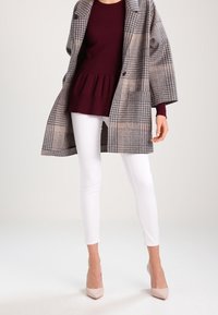 Szary i beżowy płaszcz w kratę, bordowy top z baskinką, białe legginsy i jasnoróżowe szpilki. Płaszcz ma luźny krój, dwa guziki i szerokie rękawy.