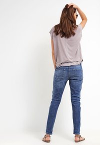 Szary top z krótkim rękawem w połączeniu z niebieskimi obcisłymi dżinsami, z tylnymi kieszeniami i gładką teksturą. Założony z brązowymi sandałami.