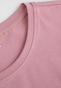 Różowa bawełniana koszulka z okrągłym dekoltem, o gładkiej fakturze i stębnowanych brzegach. Materiał jest lekki i elastyczny.