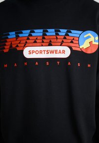 Sudadera negra con gráficos llamativos en azul, rojo y blanco. El texto incluye "SPORTSWEAR" y "MANASTASH." Incluye un ícono de una figura en movimiento.