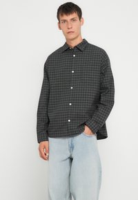 Svart rutet skjorte med hvit rutemønster, med krage og lange ermer, sammen med lys blå baggy jeans.