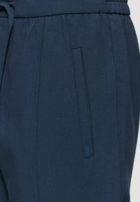 Marineblauwe broek van textuurstof, met een elastische tailleband, trekkoord en zijzak met verborgen rits.