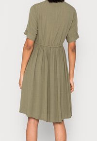 Vestido verde oliva con mangas cortas enrolladas, cintura ajustada y falda plisada. Hecho de un tejido ligero con una sutil textura vertical.