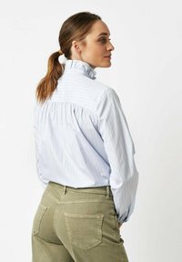 Light blue striped blouse with a high ruffled collar, pleated back, and long sleeves, paired with olive green fitted pants.
