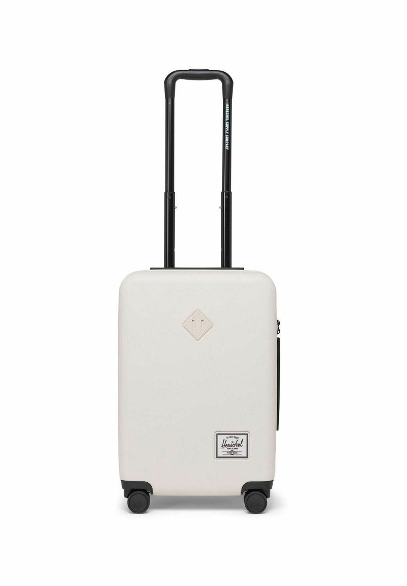 Valise rigide de couleur crème avec une surface texturée, poignée télescopique noire, quatre roues et un patch logo à l'avant.