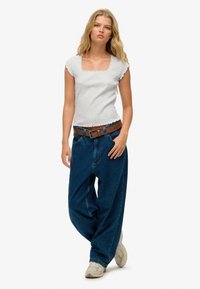 Grå kortærmet top med firkantet halsudskæring og ruffled kanter, parret med løse mørkeblå denim jeans og et brunt bælte.