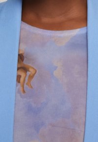 Light blue jacket with smooth texture, overlaying a graphic fabric top featuring a soft purple background and brown abstract design.