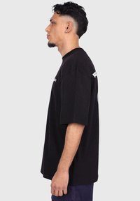 Black oversized t-shirt made of cotton, featuring short sleeves and a crew neck. Front text graphic and a colorful logo on the back.