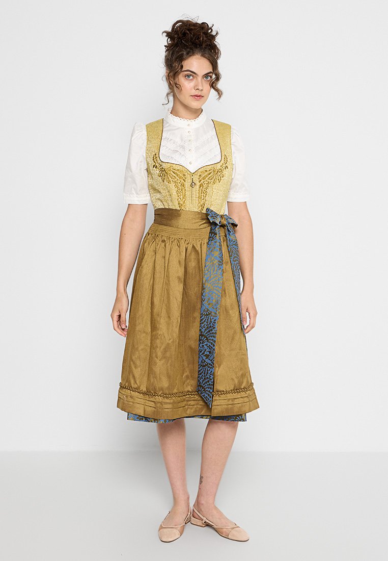 Traditionelles Kleid mit einem gelben Oberteil mit aufwendigen Mustern, weißer Bluse und einem braunen Rock mit einem blauen, gemusterten Band an der Taille.