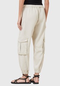 Beige cargobroek met een elastische tailleband, taps toelopende boorden en twee grote zijzakken. Zachte katoenen stof met een relaxte pasvorm.