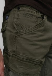 Pantalons cargo vert olive en tissu doux, avec une coupe ajustée, des poches angulaires et des coutures contrastées.