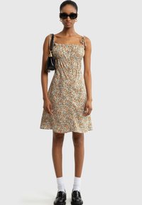 Blumenkleid mit kleinen orangefarbenen und blauen Blumen auf grünem Hintergrund. Verfügt über verstellbare Träger, ein gerafftes Oberteil und einen ausgestellt Rock.